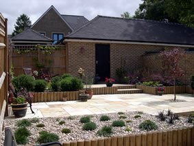 A rear garden scheme in timber and stone — raised beds, a paved sitting area and planting kept in order.