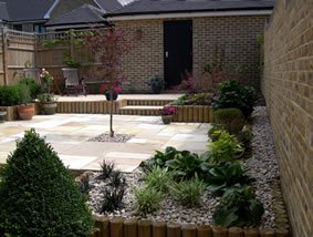 A paved courtyard with stepped planting beds and a gravel border, kept weeded and pruned on a seasonal round.