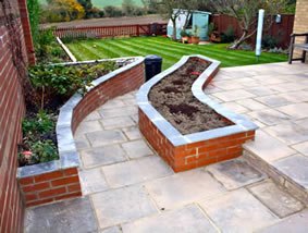 A curved brick-edged bed set into new paving with freshly laid turf behind it, photographed shortly after completion.