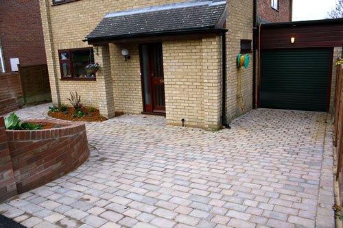 Saffron Walden — paving run right up to the garage threshold and around a curved brick planter, laid to falls so water runs off the hard standing.