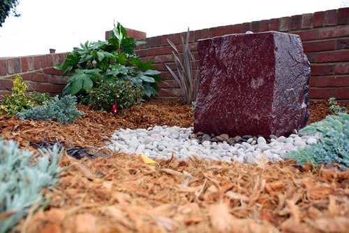 Saffron Walden — a feature stone set into a bark-mulched bed, planted with grasses and evergreens against the new brick walling.